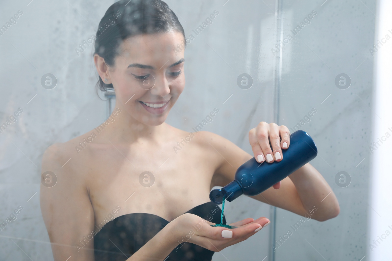 Photo of Young woman using gel in shower at home, view through glass