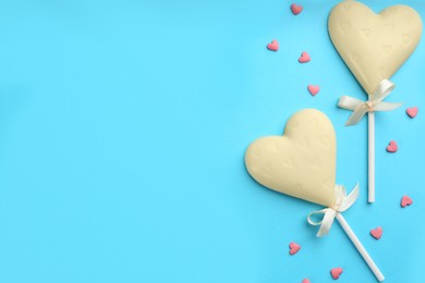 Photo of Chocolate heart shaped lollipops and sprinkles on light blue background, flat lay. Space for text
