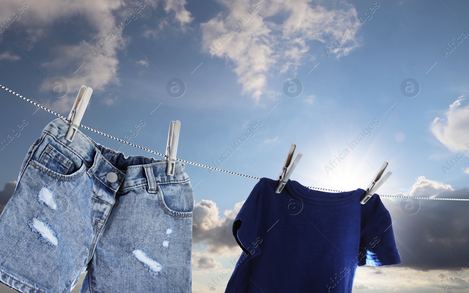 Image of T-shirt and denim shorts drying on washing line against sky