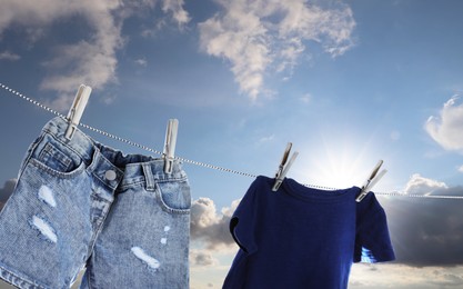T-shirt and denim shorts drying on washing line against sky