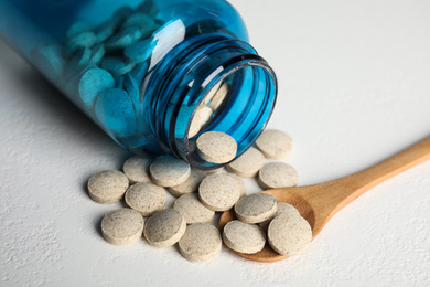 Photo of Bottle with vitamin pills and spoon on white table, closeup