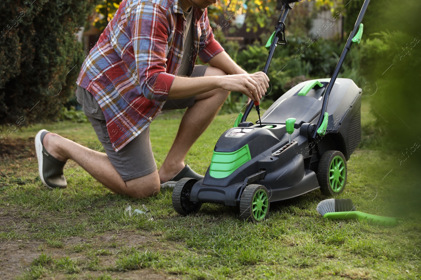 Photo of Man with screwdriver fixing lawn mower in garden, closeup