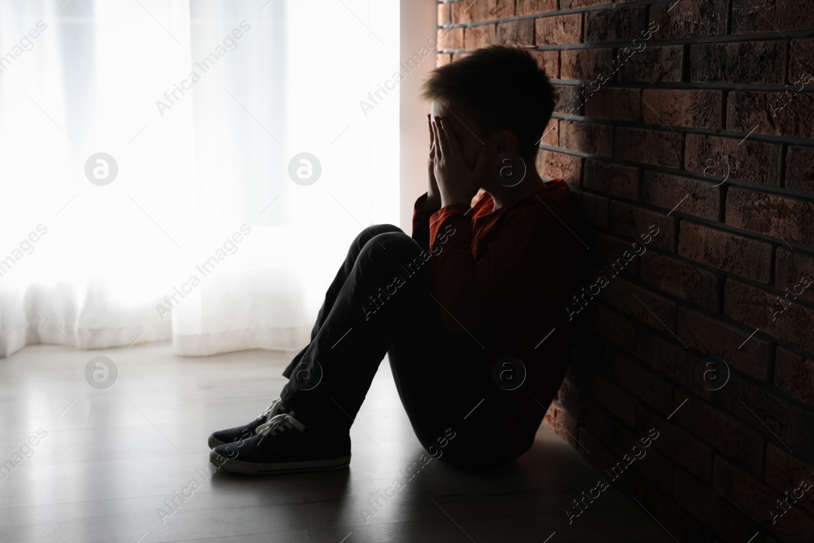 Photo of Scared little boy closing his eyes near brick wall. Domestic violence concept