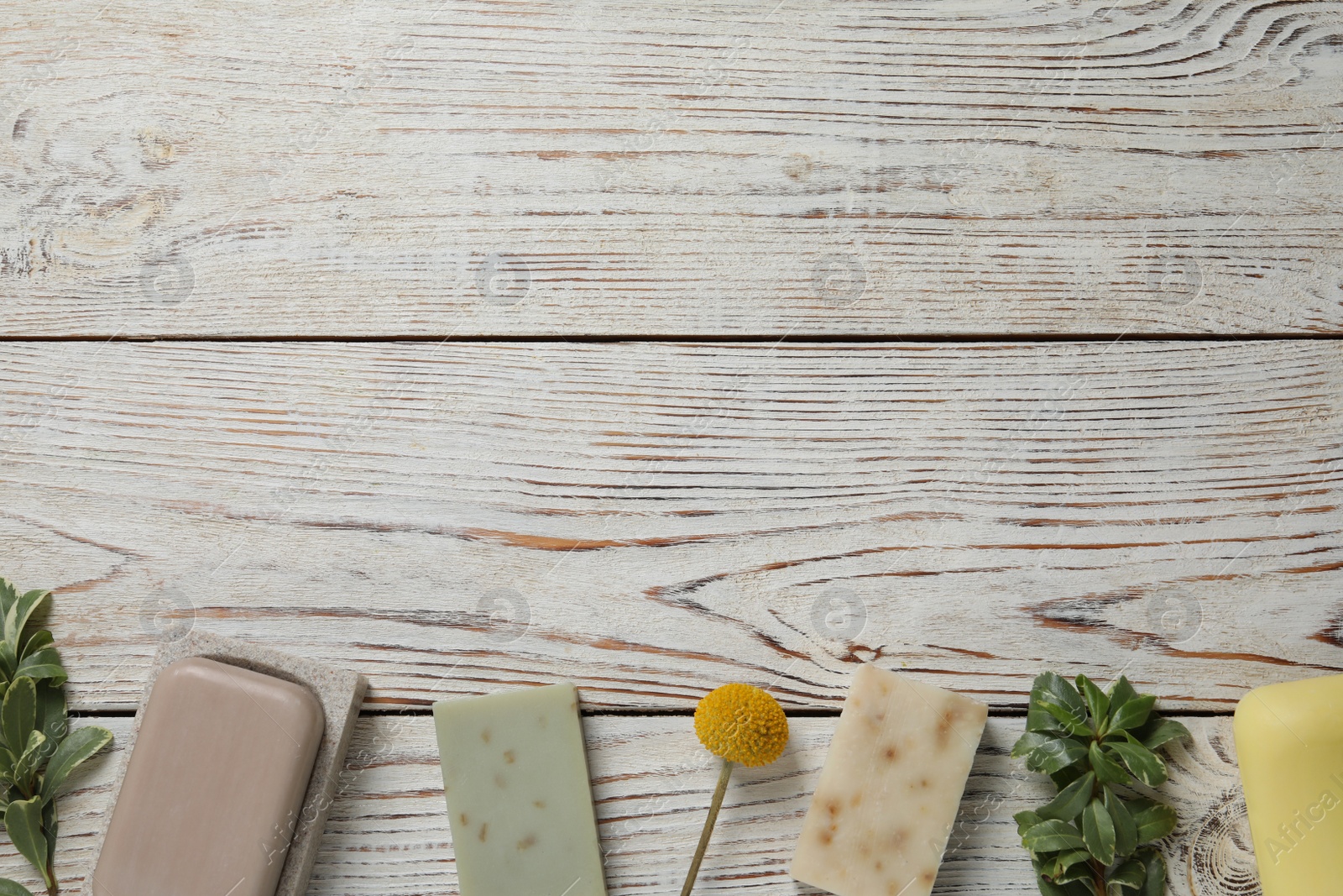 Photo of Many different soap bars and green plants on wooden table, flat lay. Space for text