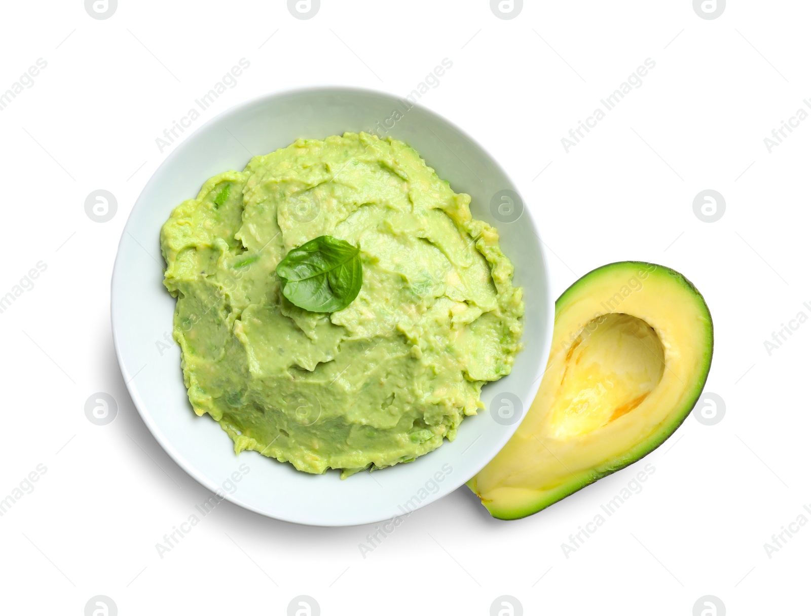 Photo of Bowl of tasty guacamole with basil and cut avocado on white background, top view