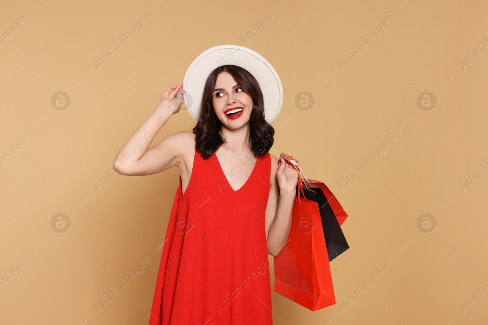 Photo of Beautiful young woman with paper shopping bags on beige background