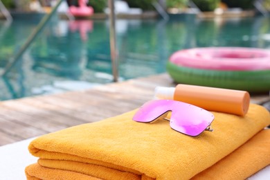 Beach towels, sunglasses and sunscreen on sun lounger near outdoor swimming pool, closeup. Luxury resort