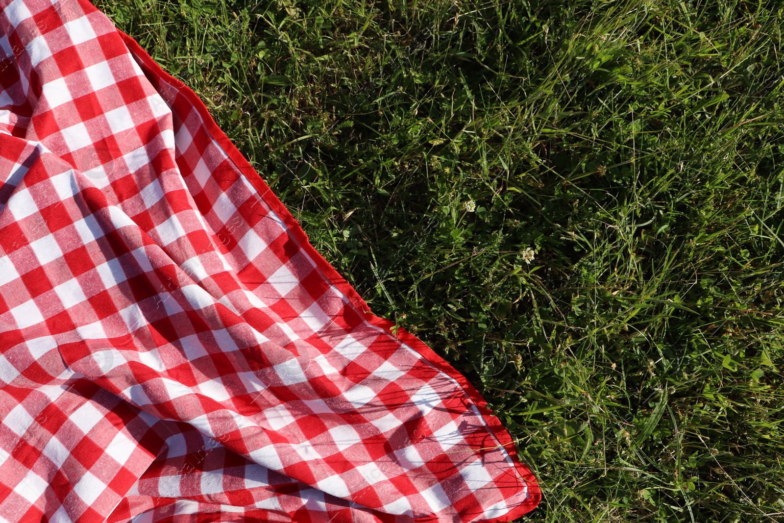 Photo of Checkered picnic tablecloth on fresh green grass, top view. Space for text