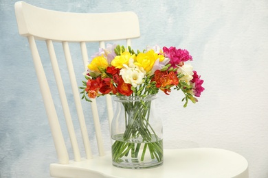 Photo of Beautiful bright freesia flowers in vase on chair