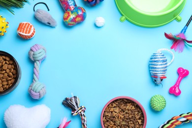 Different pet toys and feeding bowls on light blue background, flat lay. Space for text