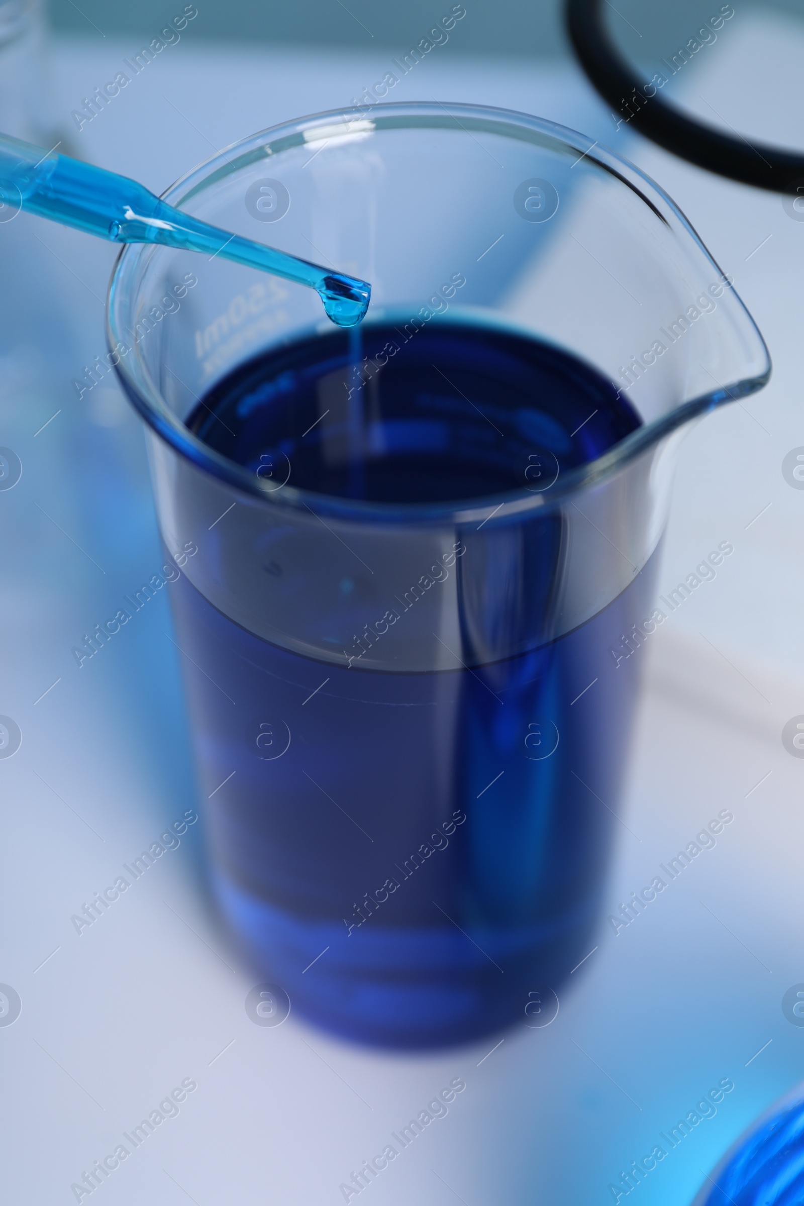 Photo of Laboratory analysis. Dripping blue liquid into beaker on white table, closeup