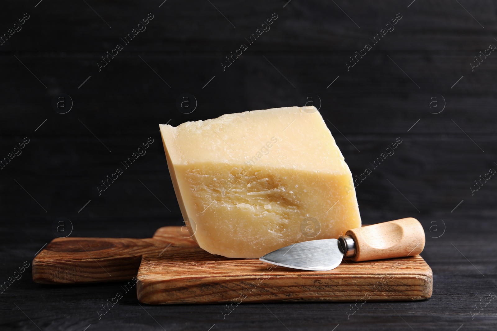 Photo of Delicious parmesan cheese with knife on black wooden table