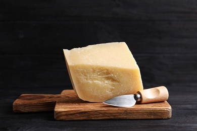 Photo of Delicious parmesan cheese with knife on black wooden table