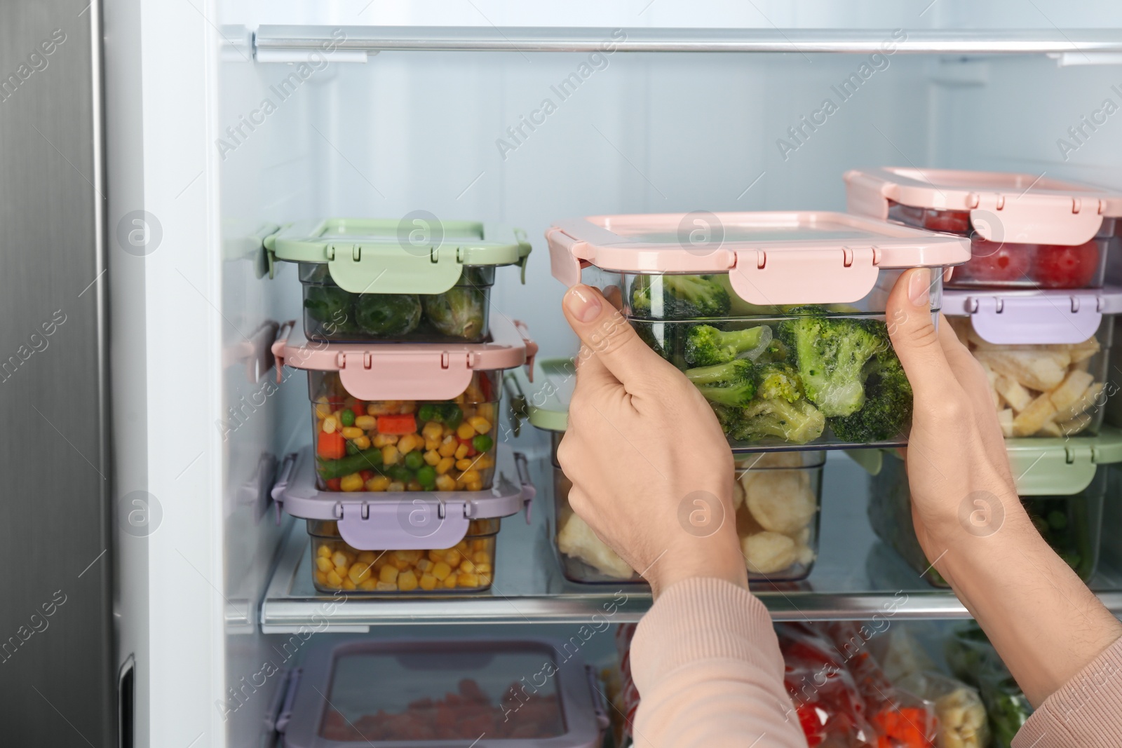 Photo of Woman taking container with frozen broccoli from refrigerator, closeup