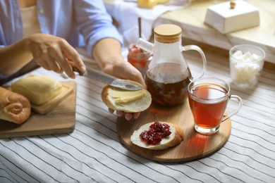 Photo of Woman spreading butter on bread near glass mug of aromatic tea indoors, closeup