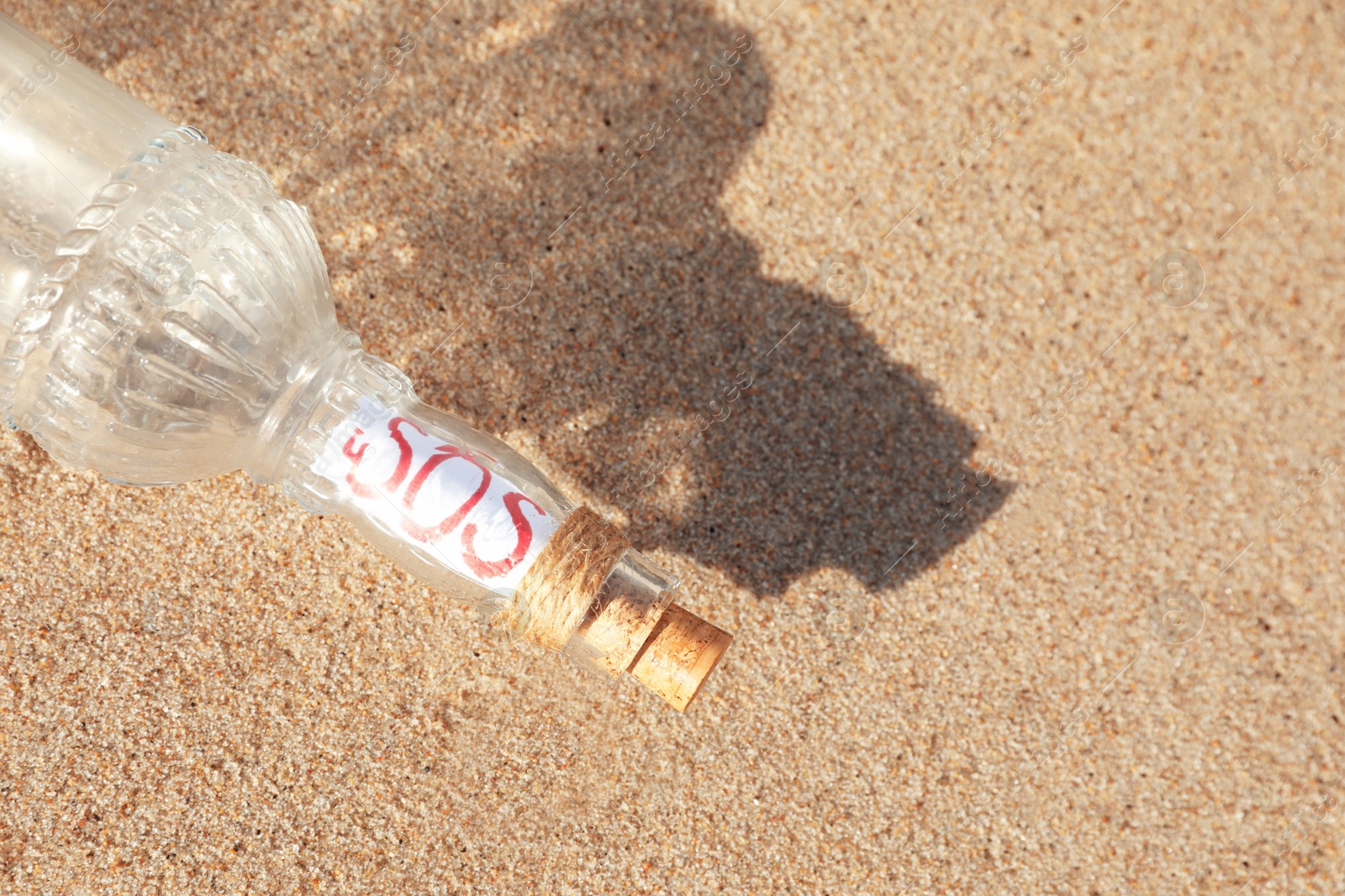 Photo of Glass bottle with SOS message on sand, top view