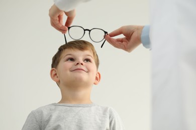 Vision testing. Ophthalmologist giving glasses to little boy indoors, low angle view