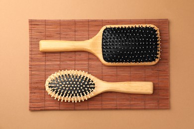 Photo of Wooden hairbrushes and bamboo mat on light brown background, flat lay