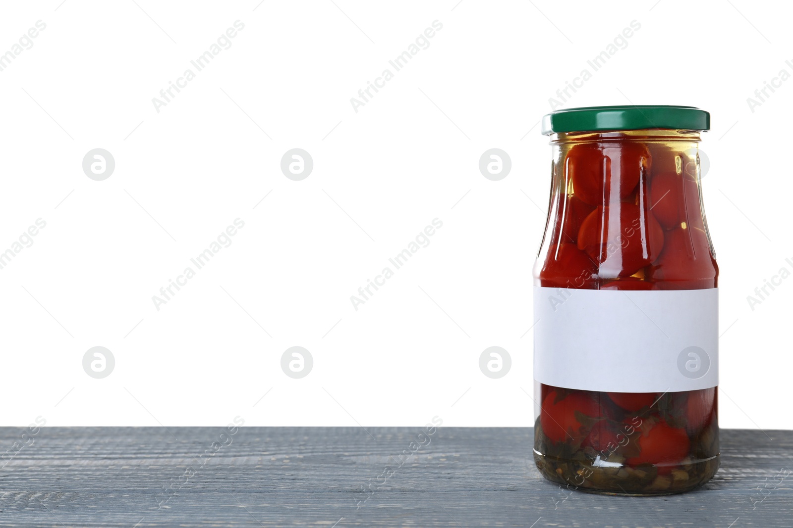 Photo of Jar of pickled cherry tomatoes with blank label on blue wooden table against white background. Space for text