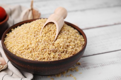 Bowl and scoop with raw bulgur on white wooden table, closeup