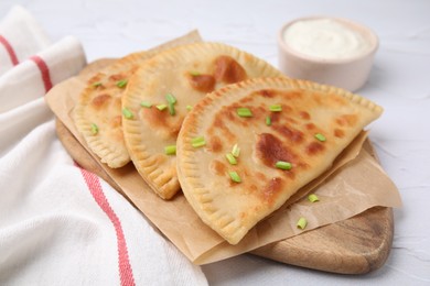 Photo of Delicious fried chebureki with cheese, green onion and sauce on white textured table