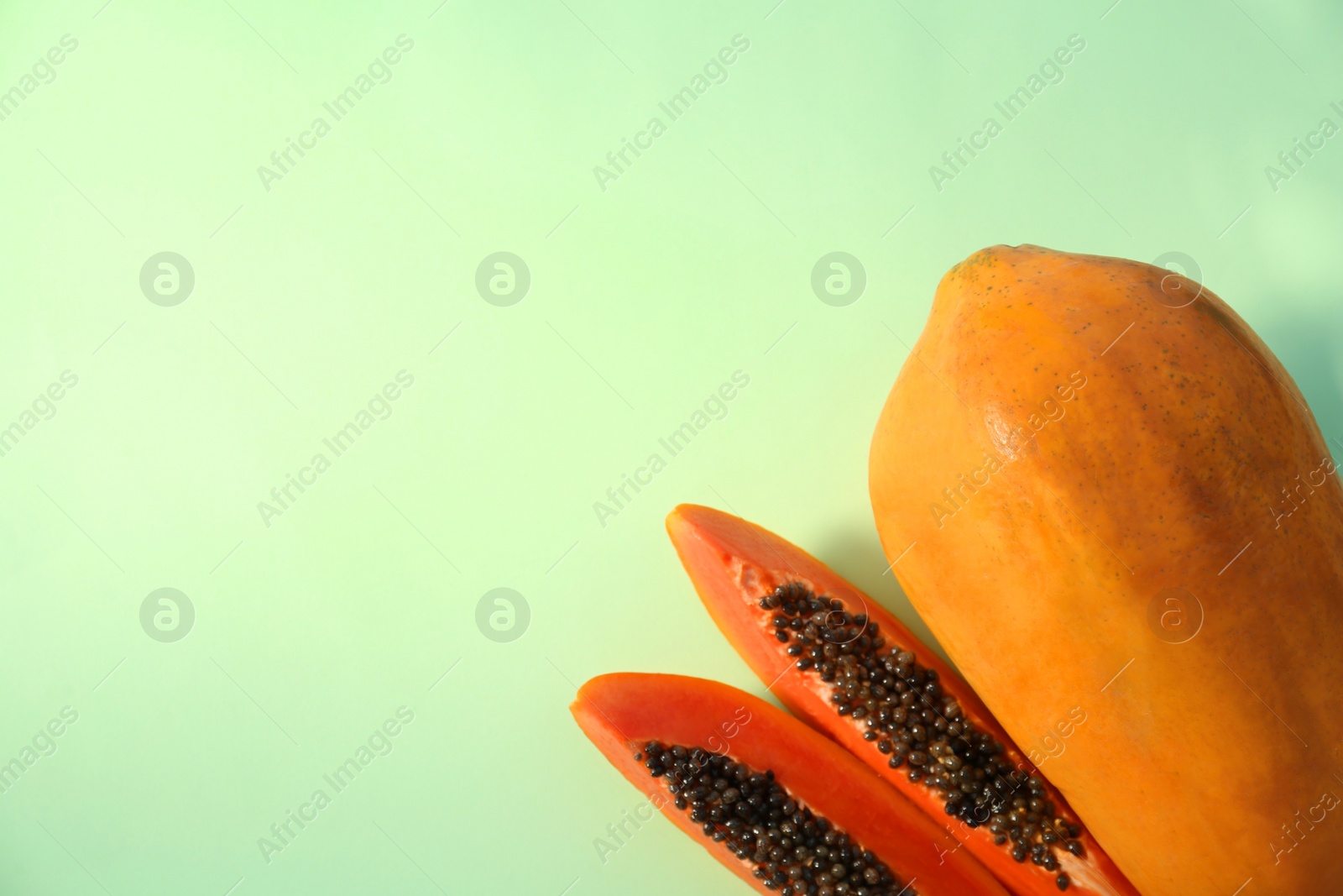 Photo of Fresh ripe cut and whole papaya fruits on light green background, flat lay. Space for text