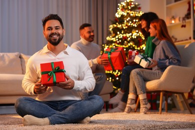 Photo of Christmas celebration in circle of friends. Happy young man with gift box at home, selective focus