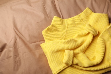 Photo of Beautiful yellow warm sweater on brown bedsheet, top view. Space for text