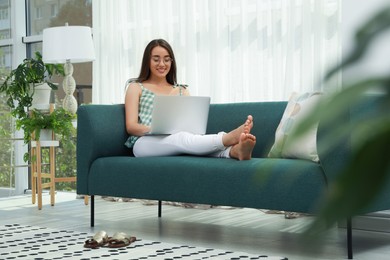 Photo of Young woman using laptop on sofa at home. Internet shopping