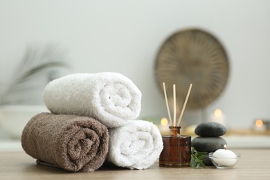 Spa composition. Rolled towels, aroma diffuser, massage stones and burning candle on wooden table indoors, closeup