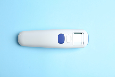 Photo of Modern non-contact infrared thermometer on light blue background, top view