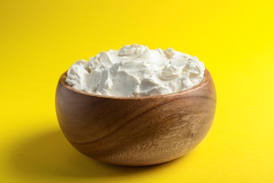 Photo of Bowl of tasty cream cheese on yellow background