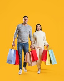 Photo of Happy couple with paper bags on yellow background. Christmas shopping
