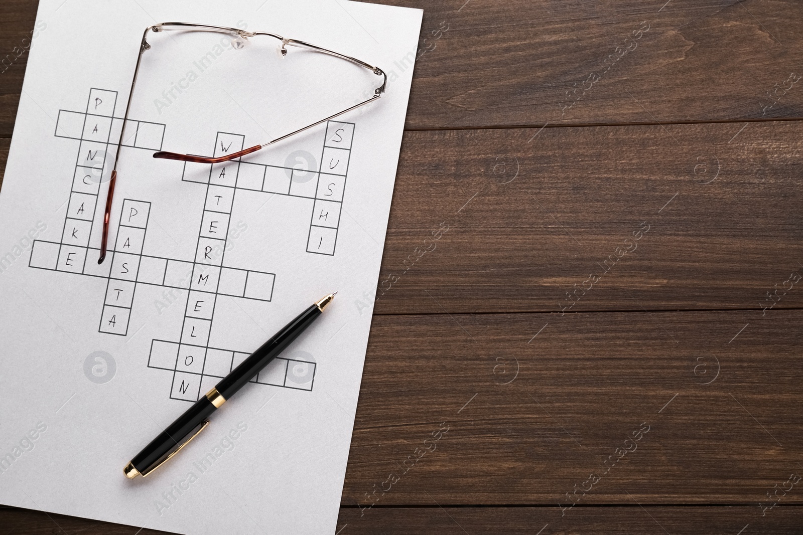 Photo of Crossword with answers, glasses and pen on wooden table, top view. Space for text
