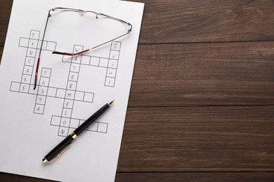 Photo of Crossword with answers, glasses and pen on wooden table, top view. Space for text