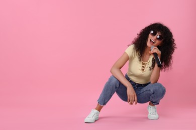 Photo of Beautiful young woman with microphone singing on pink background. Space for text