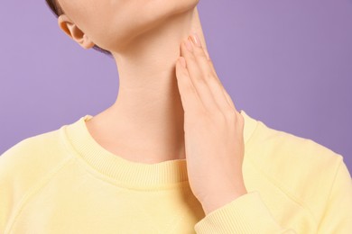 Woman with sore throat on violet background, closeup