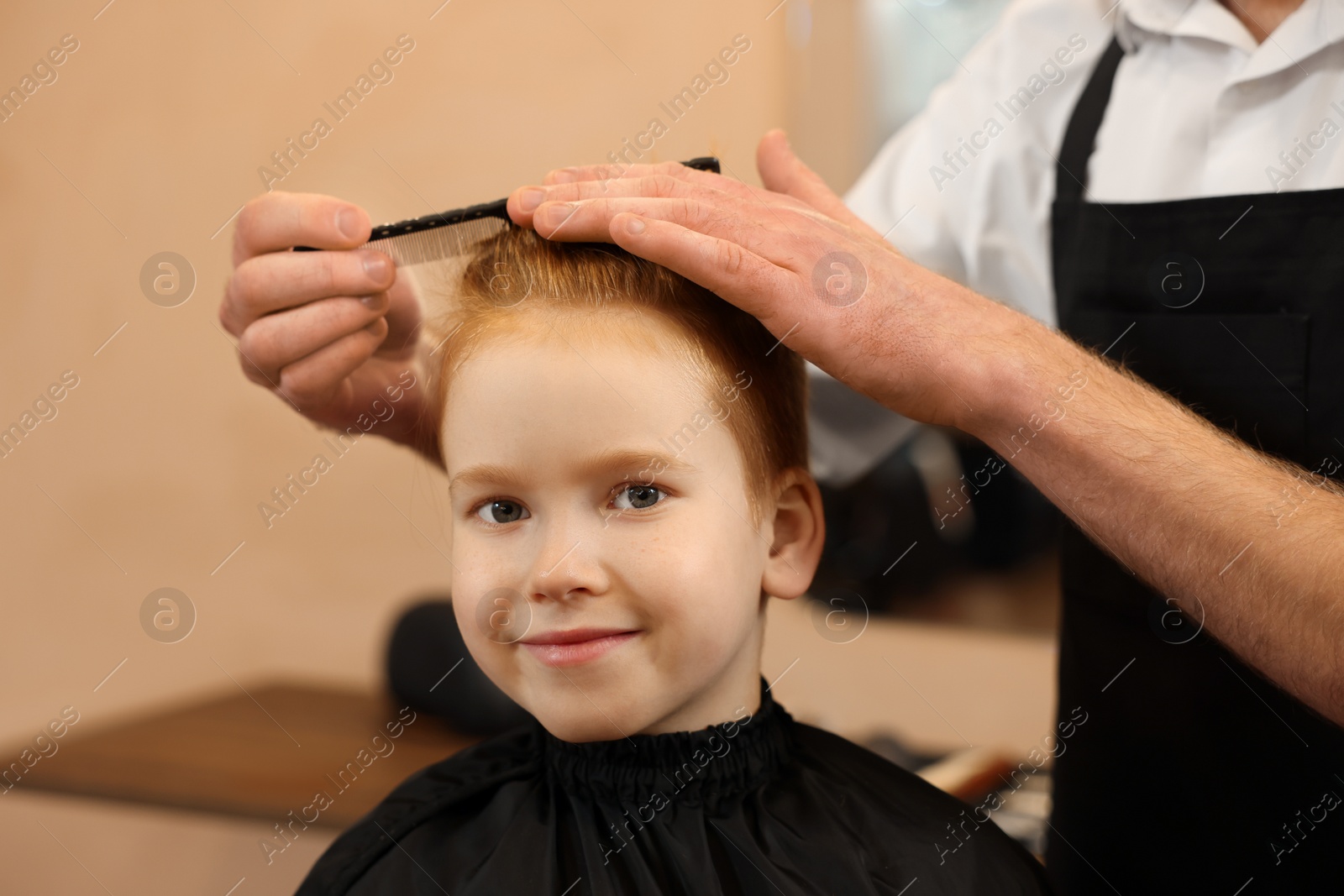 Photo of Professional hairdresser combing boy's hair in beauty salon, closeup