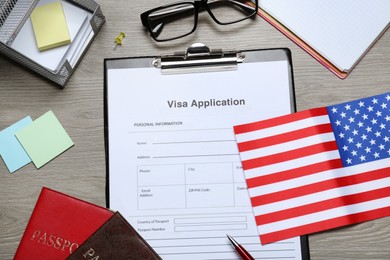 Visa application form, American flag, passports and stationery on wooden table, flat lay