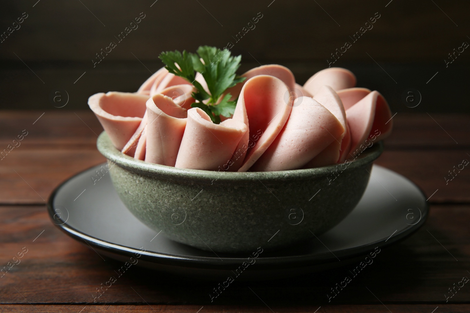 Photo of Slices of delicious boiled sausage with parsley on wooden table, closeup