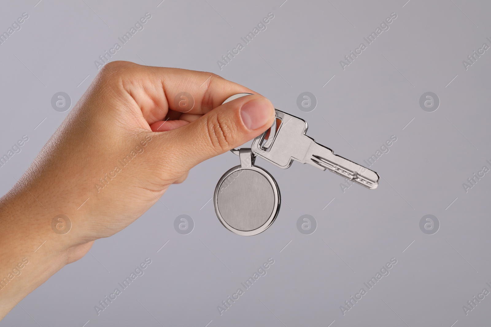 Photo of Woman holding key with metallic keychain on grey background, closeup