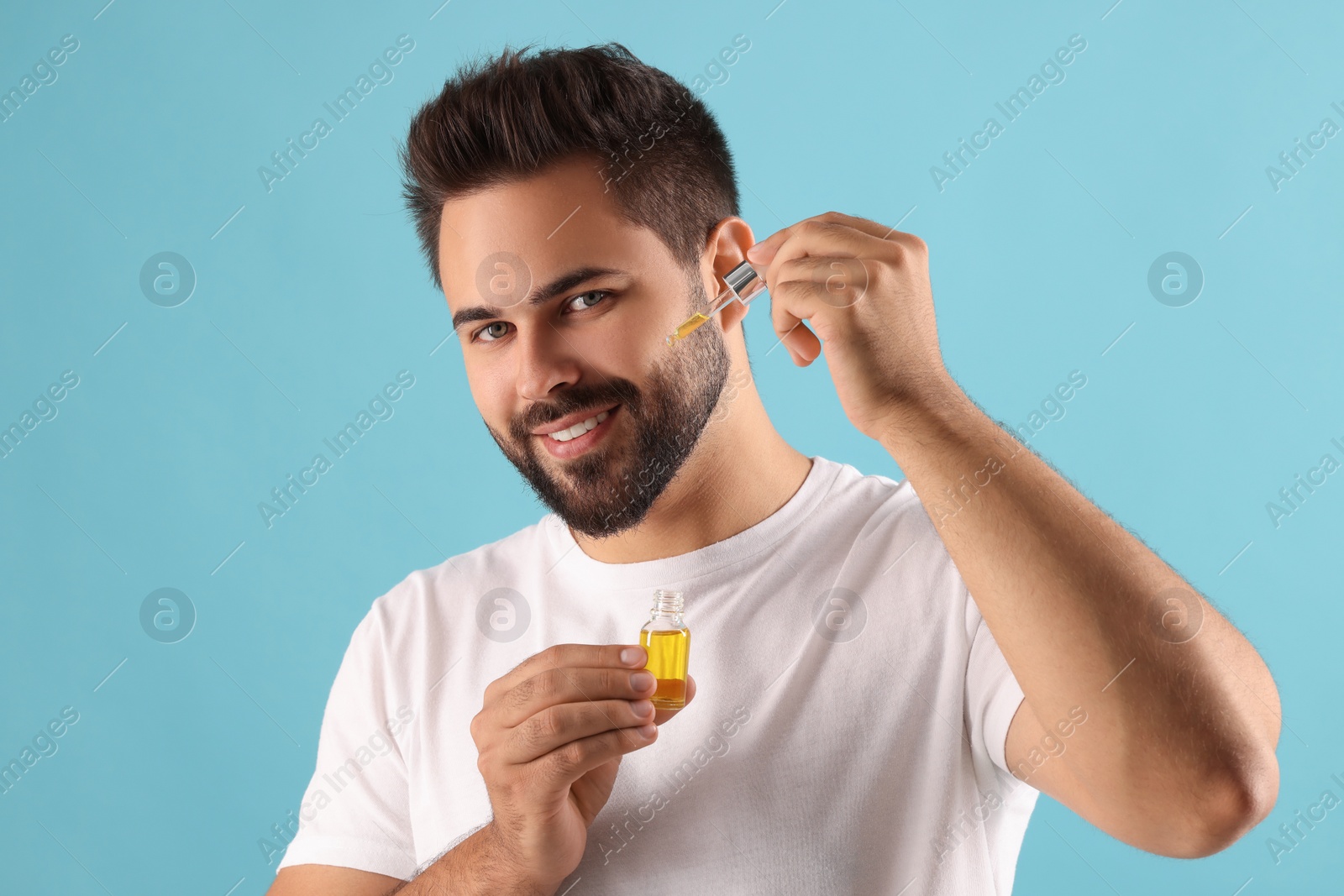 Photo of Handsome man applying cosmetic serum onto face on light blue background