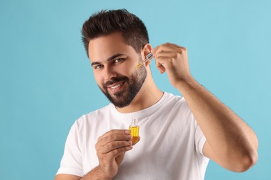 Handsome man applying cosmetic serum onto face on light blue background