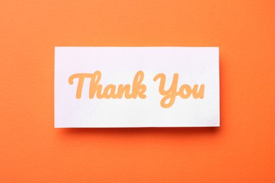 Note with phrase Thank You on orange background, top view