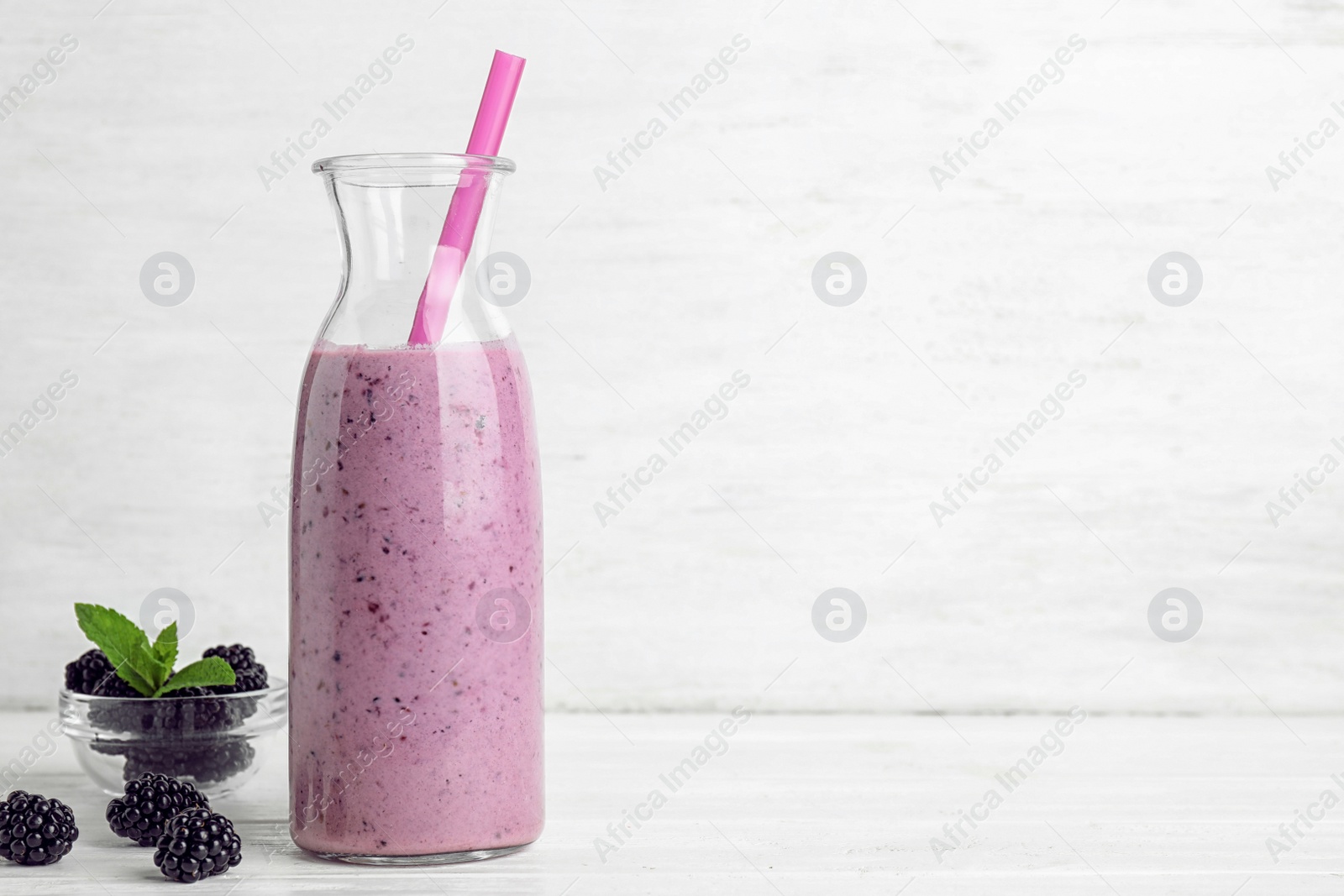 Photo of Delicious blackberry smoothie in bottle on white wooden table