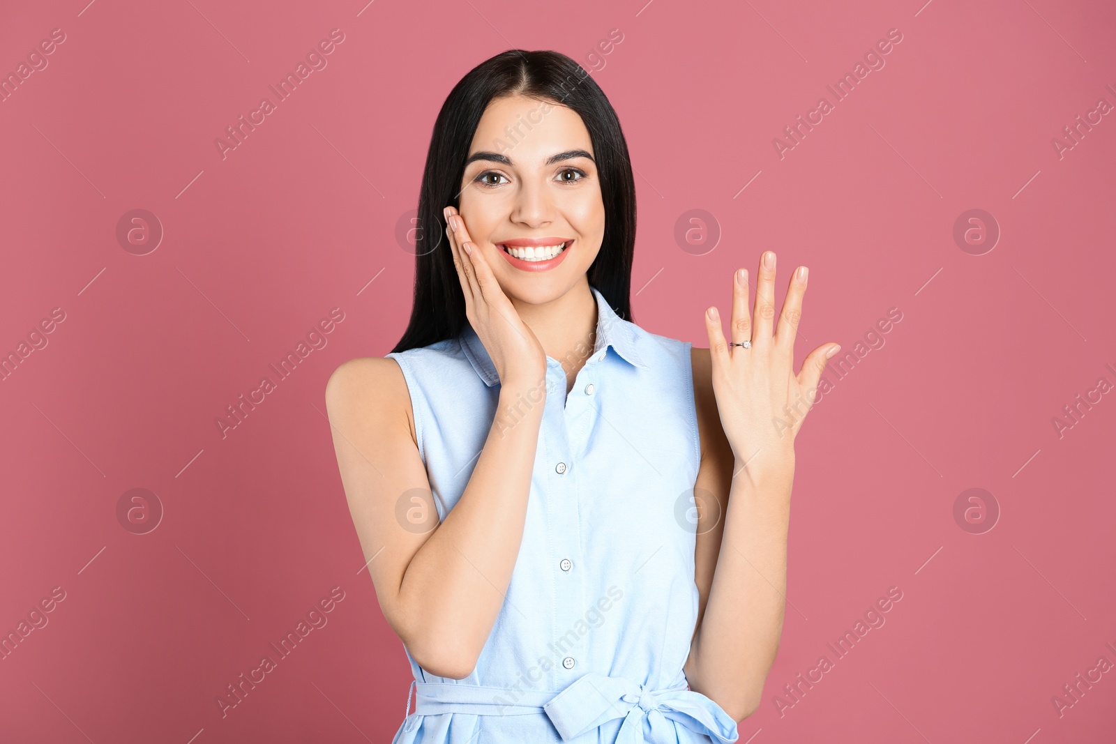 Photo of Happy young woman wearing beautiful engagement ring on pink background