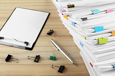 Photo of Stack of documents with binder clips, clipboard and pen on wooden table
