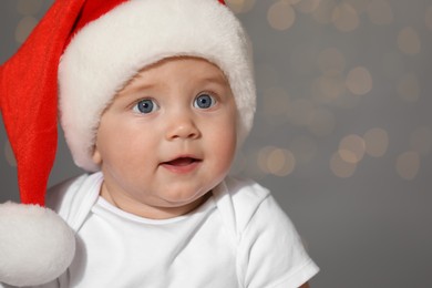 Photo of Cute baby in Santa hat against blurred lights, space for text. Christmas celebration