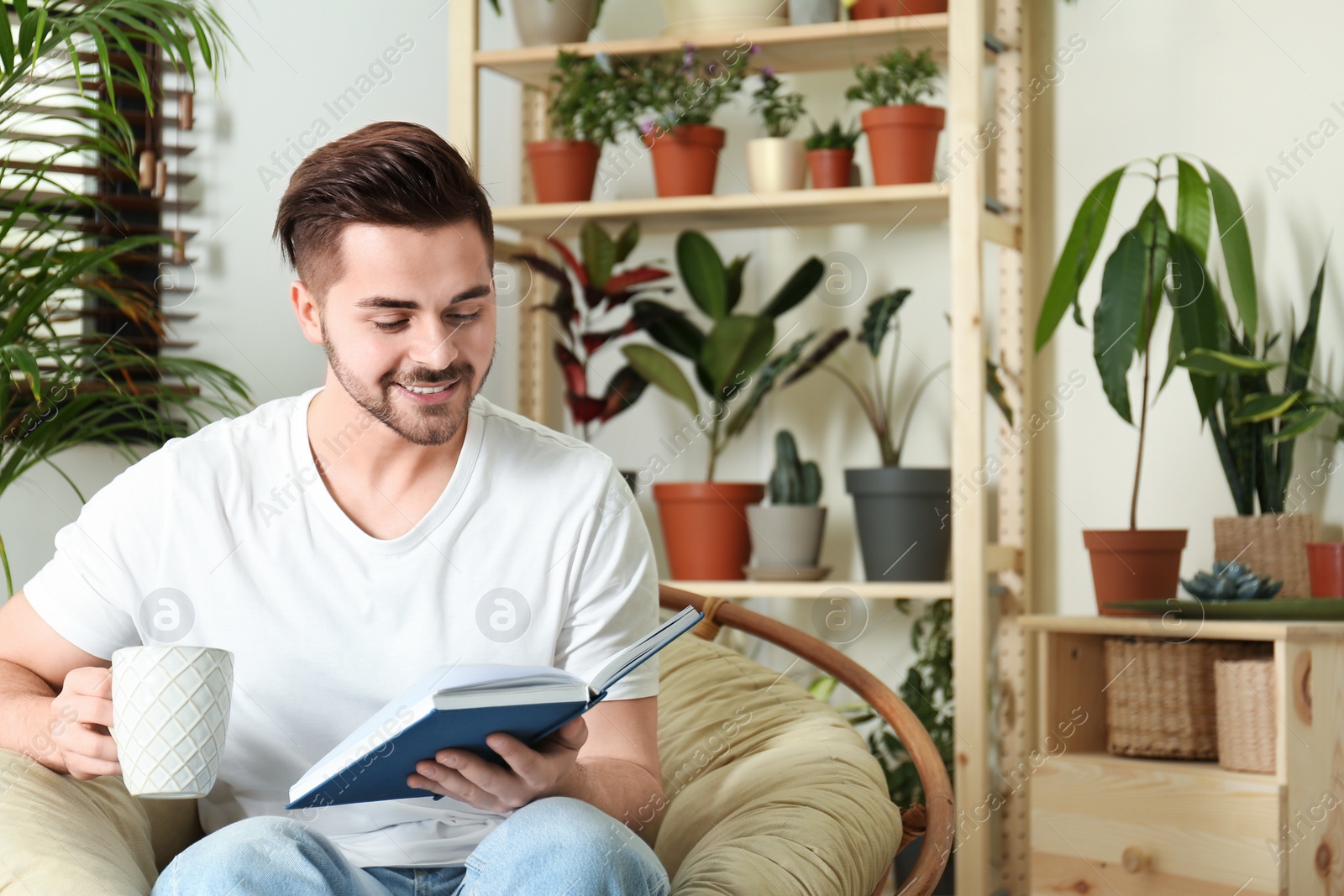 Photo of Young man reading book in room with different home plants