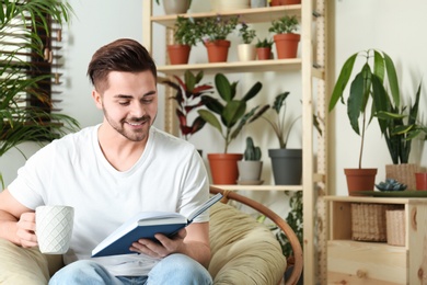 Young man reading book in room with different home plants